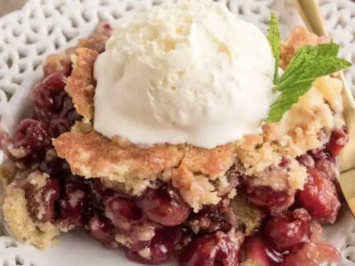 cherry dump cake on a plate, with a fork, topped with ice cream and a mint leaf.